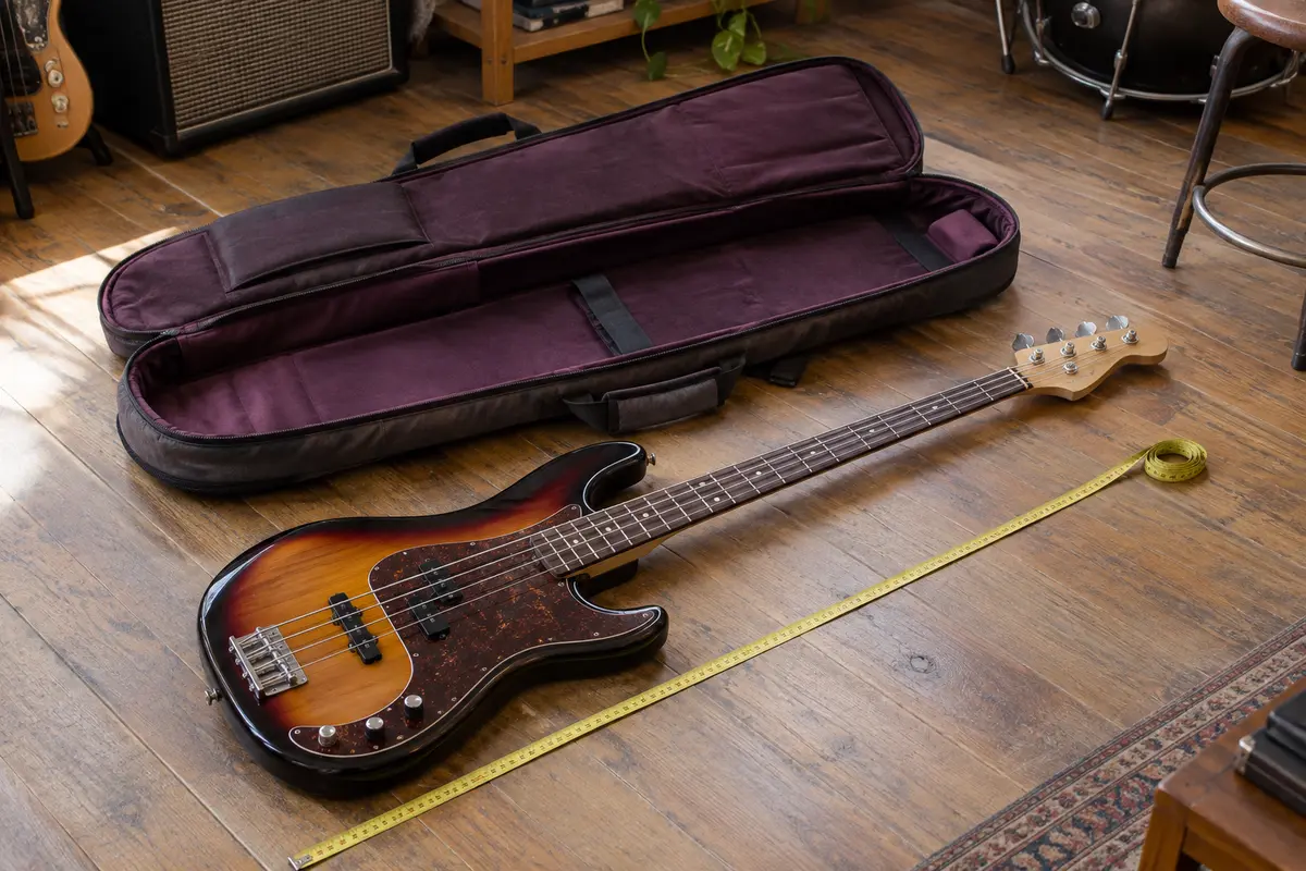 Basse électrique à quatre cordes posée près de sa housse ouverte, avec un mètre ruban le long de l’instrument