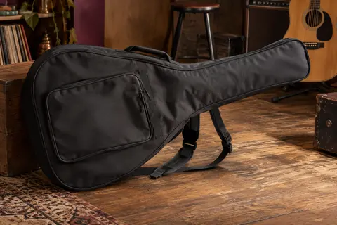Housse noire en polyester pour guitare acoustique, avec poche frontale et bretelles, posée dans un atelier musical.