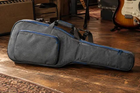 Housse grise pour guitare électrique posée sur un sol de bois, avec fermetures éclair bleues.