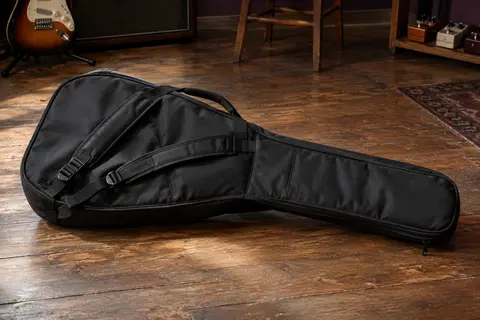 Housse noire rembourrée pour guitare électrique posée sur un sol de bois patiné dans un atelier musical