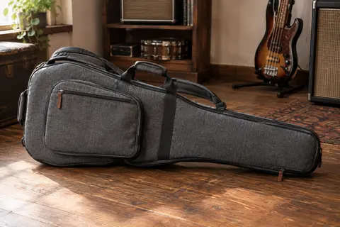 Housse grise pour basse électrique posée sur un sol de bois patiné dans un atelier musical