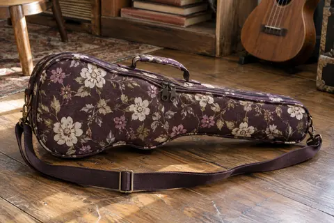 Housse en coton à motif floral pour ukulélé, avec poignée et bandoulière réglable, posée dans un atelier musical.