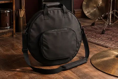 Sac rond noir rembourré pour cymbales, posé sur un sol en bois avec une cymbale partiellement visible.