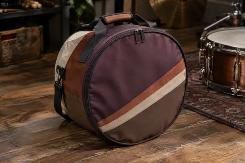 Housse Tama en nylon multicolore pour caisse claire, posée sur un sol de bois patiné dans un atelier musical.