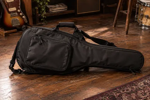 Housse noire pour guitare électrique posée dans un atelier, avec poignée, bretelles réglables et poche avant visibles.
